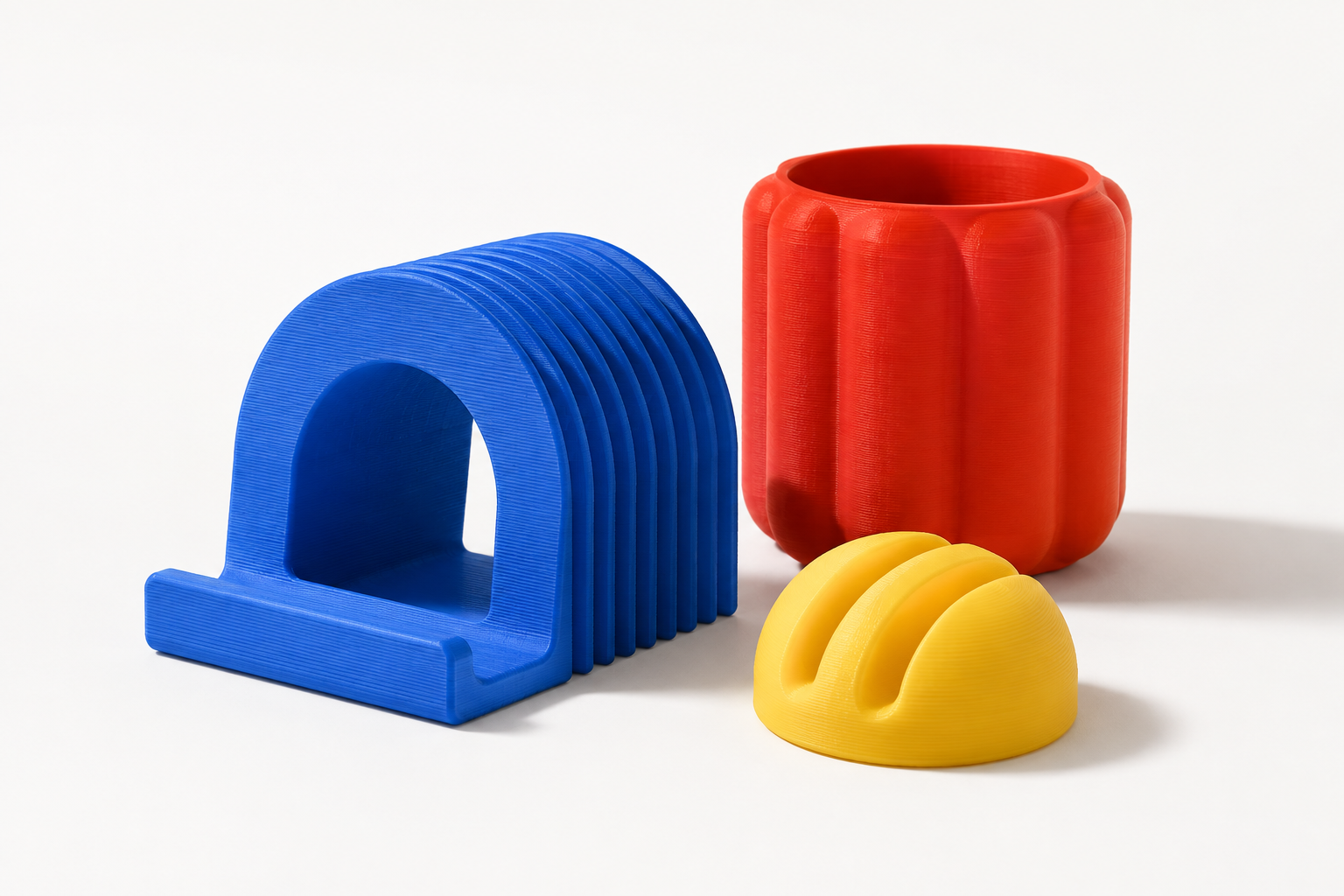 Concept render of a blue arch phone stand, red ribbed pencil cup and yellow cable organizer